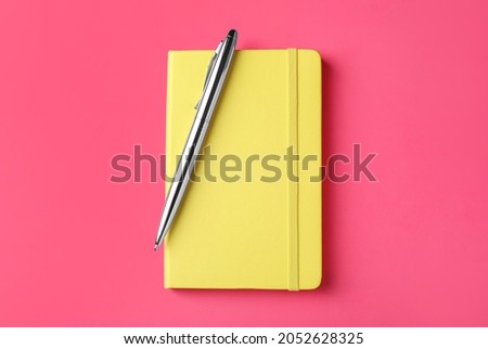 New stylish planner with hard cover and pen on pink background, top view