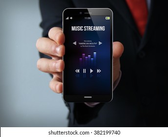 new technologies delivery concept: businessman hand holding a 3d generated touch phone with music streaming app on the screen. Screen graphics are made up. - Shutterstock ID 382199740