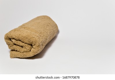 New Terry Brown Towel Rolled Up On A Gray Background. The Concept Of Cleanliness And Hygiene. Bath Accessories Made Of Cotton. Spa, Body Care. Close-up, Side View, Copy Space, Selective Focus.