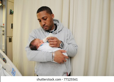 New Tired Family Father Holding Feeding Newborn Infant Baby In Hospital Room Just After Birth