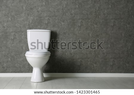 New toilet bowl near grey wall indoors. Space for text