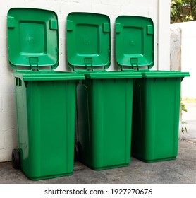 A new unbox green large bins ready to use on footpath and white concrete wall.