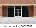 A new unoccupied generic store front, business or professional office space in a contemporary strip mall. Red brick with dark tinted windows in brushed aluminum frames and a double door.