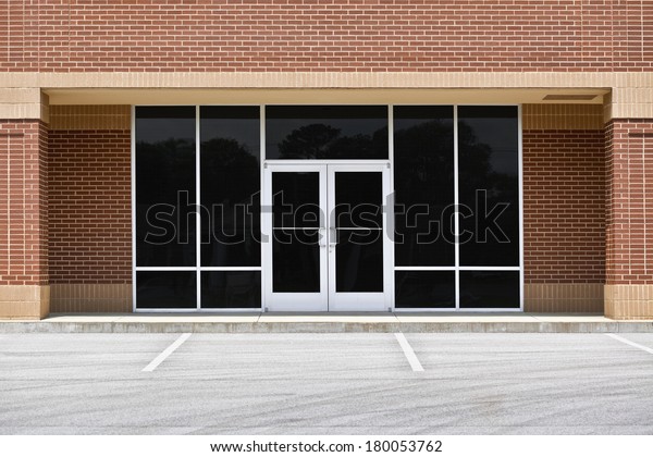 A\
new unoccupied generic store front, business or professional office\
space in a contemporary strip mall. Red brick with dark tinted\
windows in brushed aluminum frames and a double\
door.