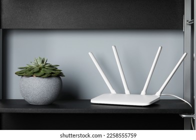 New white Wi-Fi router near potted plant on black shelf - Shutterstock ID 2258555759