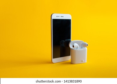 New wireless headphones in the charging box and smartphone, yellow background. air pods convenient contactless headphones, stylish bright background