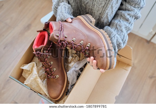 New womens leather\
brown waterproof hiking winter autumn boots in hands of female,\
trendy footwear for winter. Unpacking shoes, shopping online from\
home, shoe fashion store