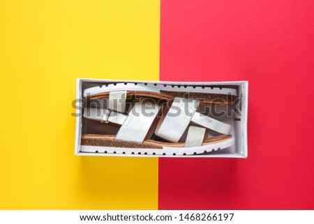 New women's leather sandals in a box on a red-yellow background. Top view. Minimalistic fashion still life
