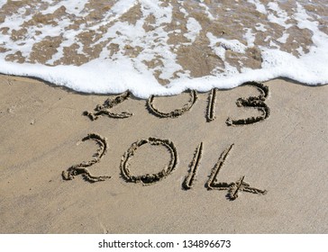  New Year 2014 is coming concept - inscription 2013 and 2014 on a beach sand, the wave is starting to cover the digits 2013