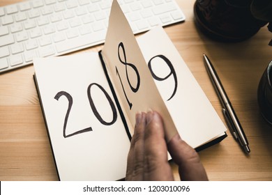 New Year 2019 is coming concept. Female hand flips notepad sheet on wooden table. 2018 is turning, 2019 is opening, toned