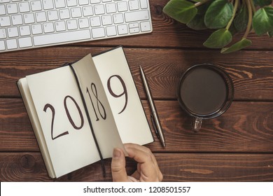 New Year 2019 is coming concept. Female hand flips notepad sheet on wooden table. 2018 is turning, 2019 is opening, top view, toned