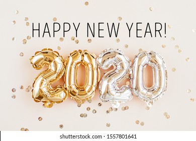 New year 2020 celebration. Gold and silver foil balloons numeral 2020 and confetti on pink background. Flat lay