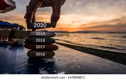 New Year 2020 is coming concept. Old year 2019 change to 2020 background. Turn of old year concept. Happy new year 2020 replace 2019. New hopes, excitement with 2020. Man adding stone to pebble tower.
