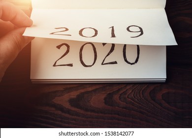 New Year 2020 coming concept. Male fingers flips notepad or calendar sheet. 2019 is turning, 2020 is opening, top view, toned