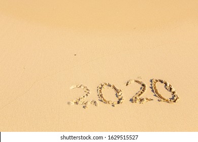 New Year 2020 is coming - inscription 2020 on a beach sand the wave is starting to cover the digits - Summer beach holiday 2020 season golden sand old year - message handwritten - empty copy space