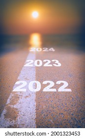 New Year 2022 To 2024 On Asphalt Road Surface With White Marking Line Leading Into Abstract Blur Sunlight And Sun. Start To Sustainable Business Strategy Concept