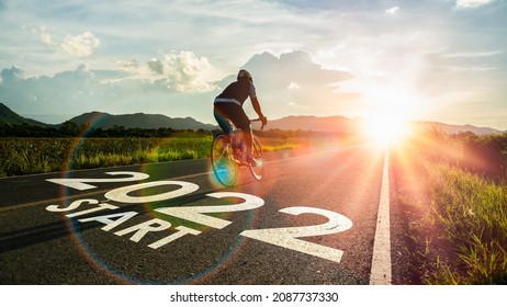 New year 2022 or start straight and beginning concept.Blurry Man ride on bike and word 2022 start written on the road at sunset add lens flare.Concept of challenge or career path,business strategy.