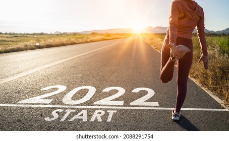 New year 2022 or start straight concept.word 2022 written on the asphalt road and athlete woman runner stretching leg preparing for new year at sunset.Concept of challenge or career path and change. - Shutterstock ID 2088291754