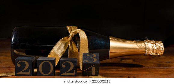 New Year 2023 2024 Sylvester New Year's Eve celebration holiday greeting card banner - Black cubes with year on sparkling wine or champagne bottle on table and black background - Shutterstock ID 2233002213