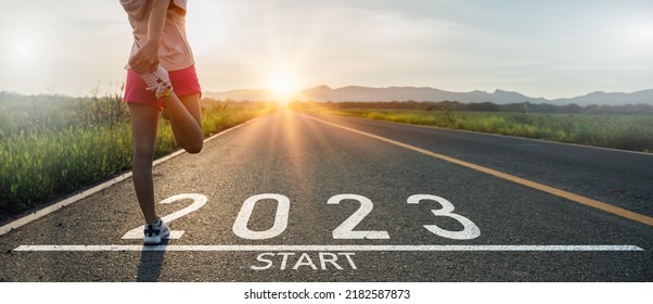 New year 2023 or start straight concept.word 2023 written on the asphalt road and athlete woman runner stretching leg preparing for new year at sunset.Concept of challenge or career path and change. - Powered by Shutterstock