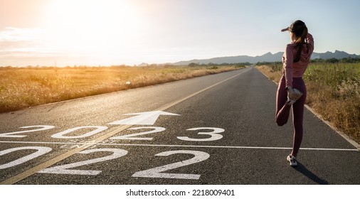 New year 2023 or start straight concept.word 2023 written on the asphalt road and athlete woman runner stretching leg preparing for new year at sunset.Concept of challenge or career path and change. - Shutterstock ID 2218009401