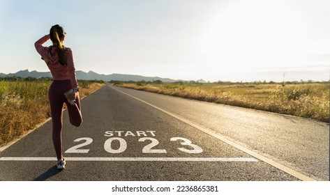 New year 2023 or start straight concept.word 2023 written on the asphalt road and athlete woman runner stretching leg preparing for new year at sunset.Concept of challenge or career path and change. - Shutterstock ID 2236865381