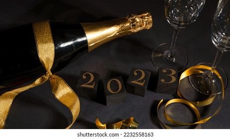 New Year 2023 New Year's Eve celebration holiday greeting card background - Black cubes with year, sparkling wine or champagne bottle and glasses on black table, top view - Shutterstock ID 2232558163