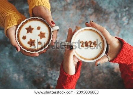 New year 2024 celebrated coffee cup with the number 2024 on frothy surface in female hands holding over rustic blue background and another one with star symbols on frothy surface. Holidays food art.