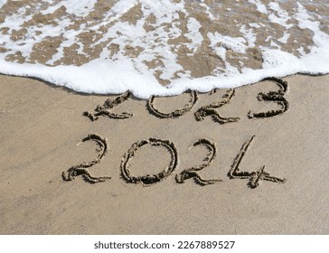 New Year 2024 is coming concept - inscription 2023 and 2024 on a beach sand, the wave is starting to cover the digits 2023