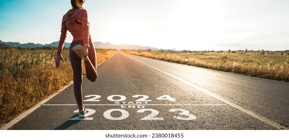 New year 2024 or start straight concept.word 2024 written on the asphalt road and athlete woman runner stretching leg preparing for new year at sunset.Concept of challenge or career path and change.
