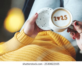 New year 2025 celebrated coffee cup with number 2025 over frothy surface holding by female hands with red nail polish and rings, dark background with blurred string lights. Holidays food art theme. - Powered by Shutterstock