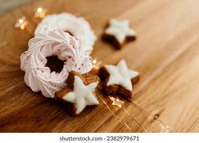 New Year background for winter cards. Gingerbread cookies in the shape of stars and pink meringue cookies lie on a brown background with Christmas lights. Delicious sweet pastries on a wood table - Powered by Shutterstock