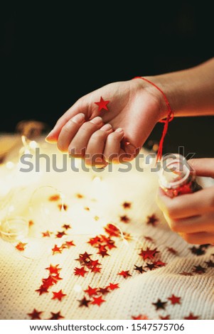 
New Year and Christmas decor, a girl holding shiny red stars in a jar with a garland on a knitted white blanket