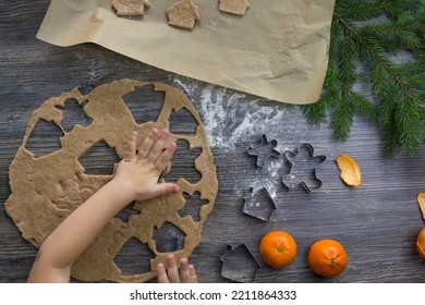 New Year and Christmas decorations on a wooden surface sprinkled with flour with tangerines and a Christmas tree. The hands of a small child make molds for cooking gingerbread in the form of a man. - Powered by Shutterstock