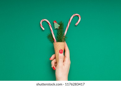 New Year Christmas Xmas holiday celebration woman hand red manicure holding waffle cone candy canes fir tree branch copy space green color paper background. Template greeting card 2019