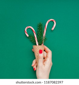 New Year Christmas Xmas holiday celebration woman hand red manicure holding waffle cone candy canes fir tree branch copy space green color paper background. Square Template greeting card 2019