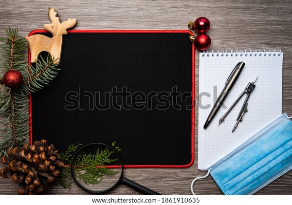 New year\
decorations flat lay. Medical mask as measure of safety at work\
place during coronavirus.Black pad background.Safe workplace with\
pen, divider, magnifier and notepad.\
