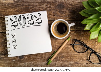 New year goals 2022 on desk. 2022 goals list with notebook, coffee cup, plant on wooden table. Resolutions, plan, goals, action, checklist, idea concept. New Year 2022 template, copy space
