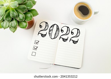 New year goals 2022 on desk. 2022 resolutions list with notebook, coffee cup on white desk. Resolutions, plan, goals, action, checklist, idea concept. New Year 2022  - Shutterstock ID 2041353212