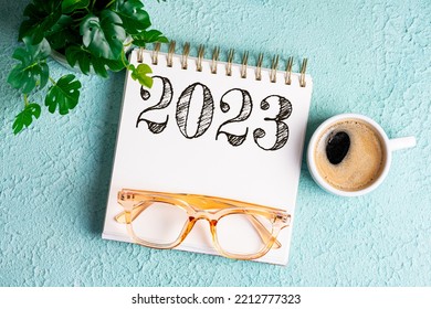 New Year Goals 2023 On Desk. 2023 Resolutions List With Notebook, Coffee Cup And Eyeglasses On Blue Background. Goals, Plan, Strategy, Business, Idea, Action Concept