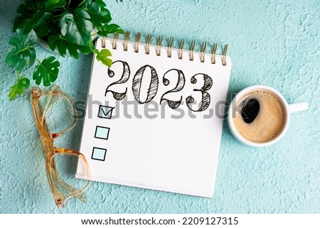 New year goals 2023 on desk. 2023 goals list with notebook, coffee cup, plant on blue table. Resolutions, plan, goals, action, checklist, idea concept. New Year 2023 template, copy space