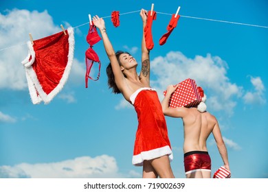New year guy with muscular body on blue sky. Christmas man and woman family. Couple in love of man and girl hanging clothes for drying. Laundry and dry cleaning. Xmas red costume on rope with pin. - Shutterstock ID 719002639
