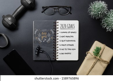 New Year Healthy Goals And Resolutions Concept. 2020 New Year's Goals Written On  Notebook Paper, And Dumbbells On Black Background, Fitness, Sport And Health Concept, Top View