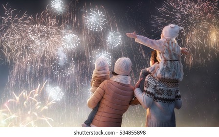 New Year holiday  Happy family  parents   daughters children girls are watching fireworks  The child sits the shoulders his father snowy winter walk in nature  Holidays winter season 