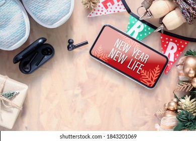 New Year New Life Resolutions Fitness Healthy Goals Concept. New Year New Life Text On Mobile Phone On Table With Sport Shoes, Wireless Earphone,  And Christmas Ornaments. Mock Up Smartphone