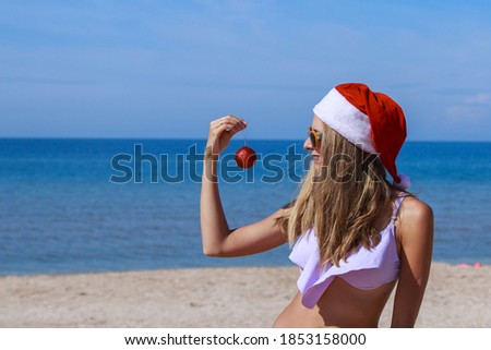 new year on the beach. funny girl in a Santa hat with a Christmas tree toy in her hands. Holiday decorations