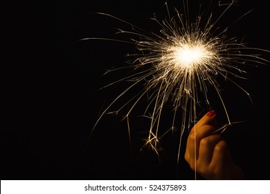 New year party burning sparkler closeup in female hand on black background. Woman holds glowing holiday sparkling hand fireworks, shining fire flame. Christmas light.