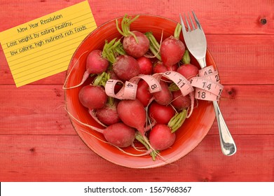 New Year Resolution (Lose Weight By Eating Healthy, Low Calorie, High Nutrient Rich Foods) On Index Card Next To Bowl Of Radishes And Fork With Measuring Tape On Red Stained Wood Table