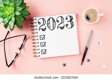 New year resolutions 2023 on desk. 2023 resolutions list with notebook, coffee cup on pink background. Goals, resolutions, plan, action, checklist concept. New Year 2023 template, copy space