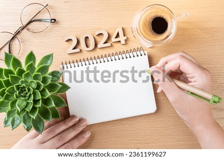 New year resolutions 2024 on desk. 2024 goals - hands and notebook, coffee cup, plant on wooden table. Resolutions, plan, goals, action,  idea concept. New Year 2024 resolutions, copy space Foto d'archivio © 